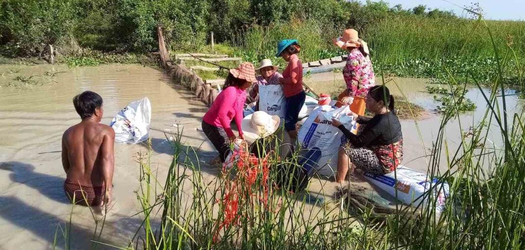 Un grupo de mujeres de pie en una pequeña masa de agua fangosa trabajando en una barrera utilizada para la gestión de la pesca.