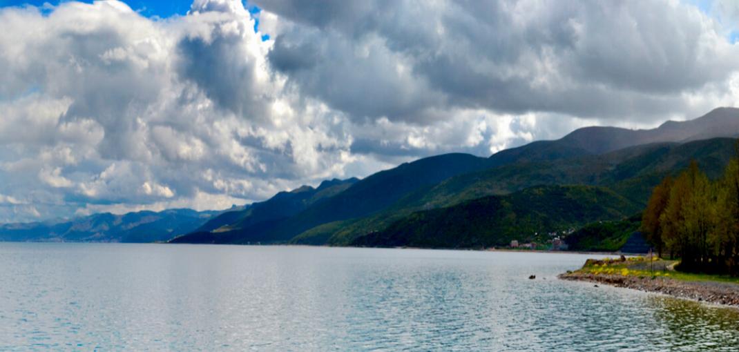 Vue sur l'eau avec des montagnes luxuriantes en arrière-plan, des nuages ​​et un ciel bleu vif.