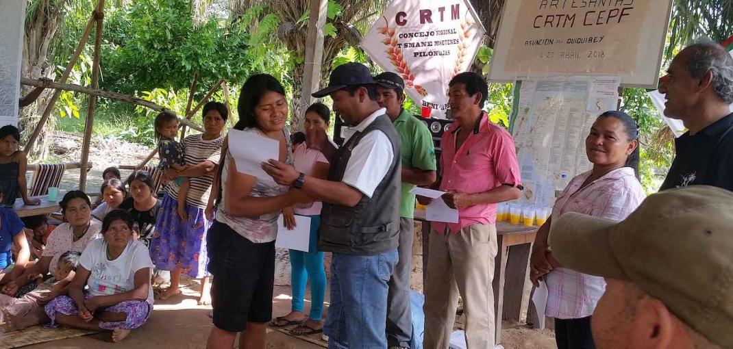 Un hombre le entrega un certificado a una joven sonriente mientras está de pie frente a un grupo debajo de una carpa.