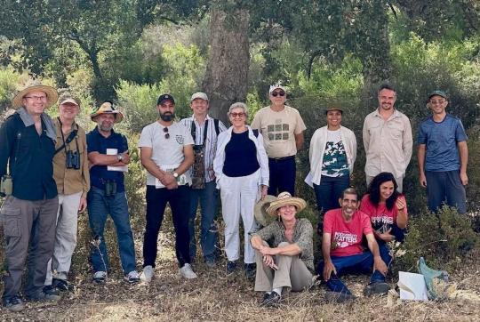 Un grupo de mujeres y hombres posan para una fotografía grupal en una zona boscosa.