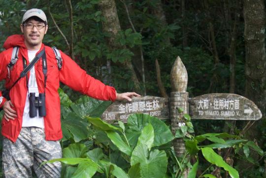 Un hombre se para al lado de una señal de sendero en un bosque.