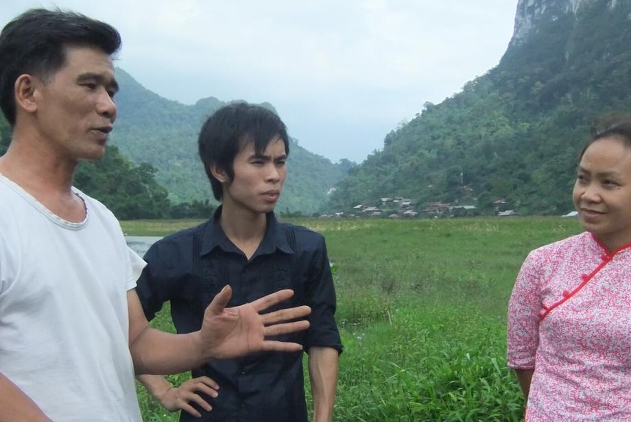 Two men and one woman having a discussion in the foreground, lush landscape in the background.