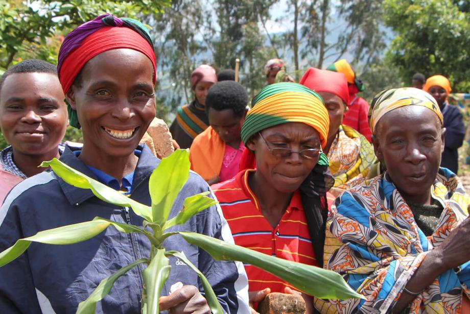Community members in bright clothing. Woman in front is smiling and holding plant.
