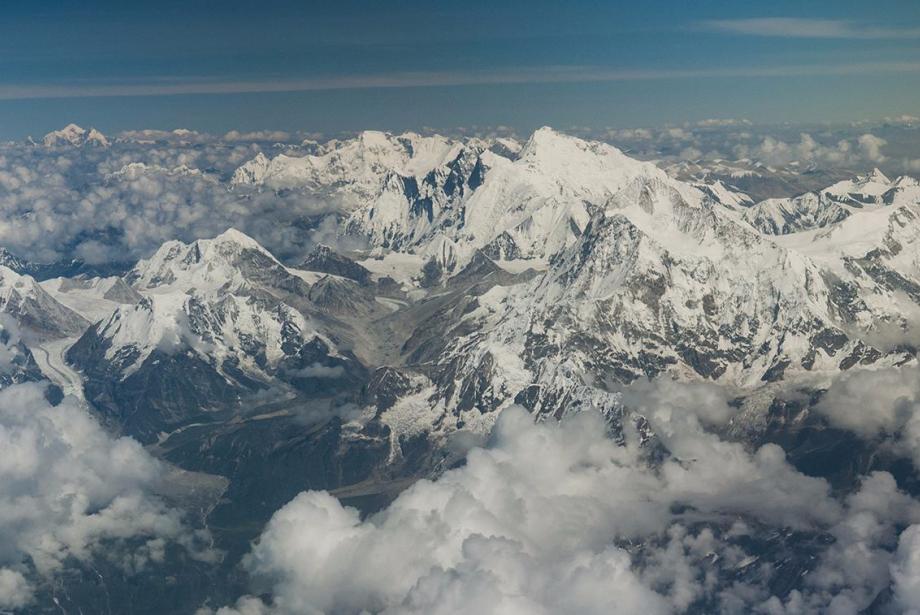 Aerial view of snowy mountains with smattering of clouds.