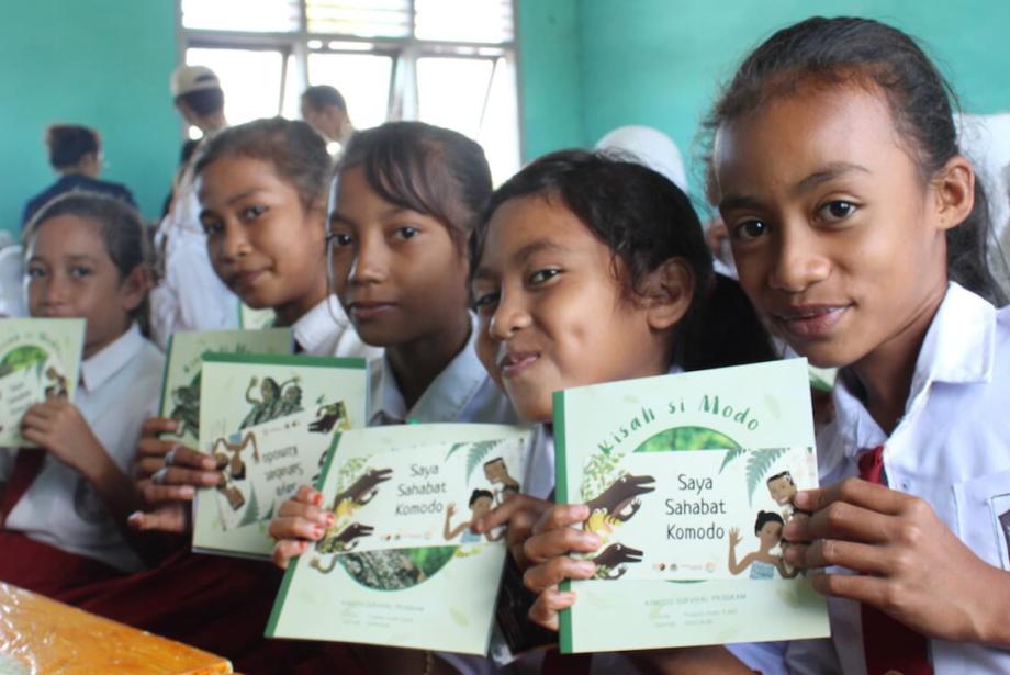 Cinco niñas sosteniendo libros educativos sobre el dragón de Komodo.