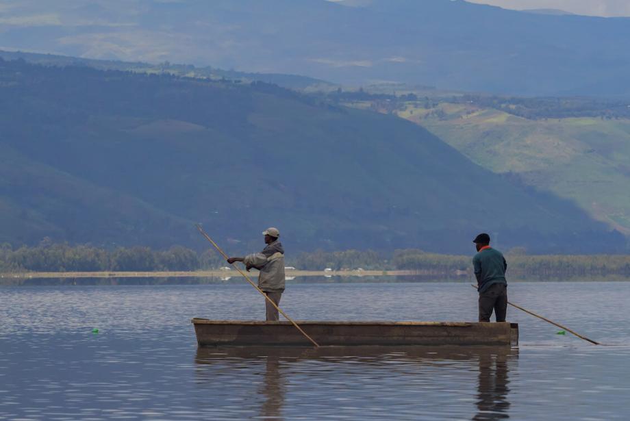 Two men standing in small boat, using long sticks to move forward.
