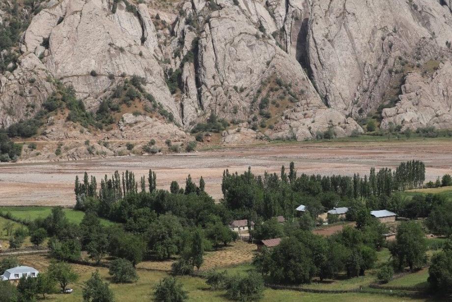 Brown river and mountains in background, small village dotted with trees in foreground