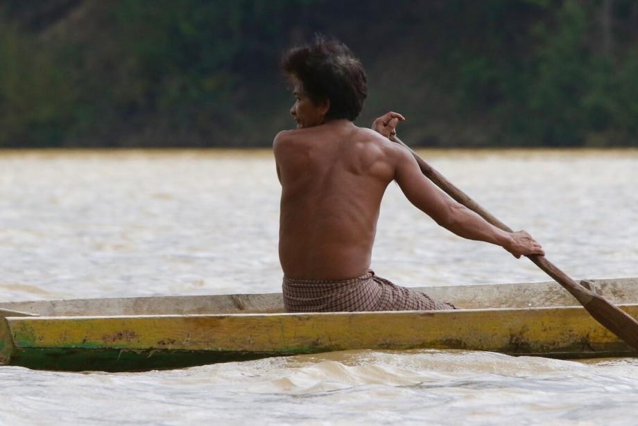 Hombre remando en canoa de madera, mira detrás de él.