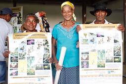 Two women and one man standing, smiling at camera. Two hold up matching posters with pictures of biodiversity.