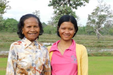 Dos mujeres sonrientes se paran frente a los arrozales verdes y al bosque.