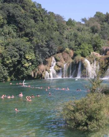 People swimming in emerald green water, series of waterfalls in the background.