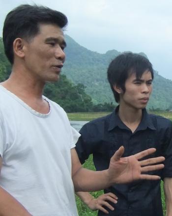 Two men and one woman having a discussion in the foreground, lush landscape in the background.