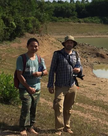 Dos hombres parados junto a un cuerpo de agua de color verde oscuro.