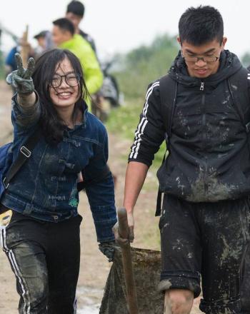 Teenagers smiling, one holding peace sign, carrying trash bags
