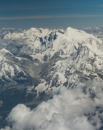Aerial view of snowy mountains with smattering of clouds.