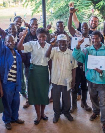 Group of about 10 standing with certificates, giving thumb's up to camera.