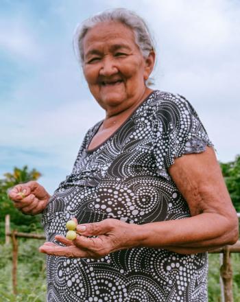 Woman standing outdoors, smiling, holding a couple small green things in her hand.