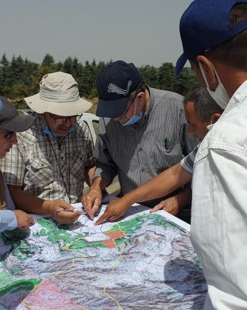 Six people outside standing around a map, pointing to various parts.