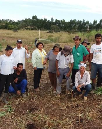 About a dozen people standing in dirt area ready for planting.
