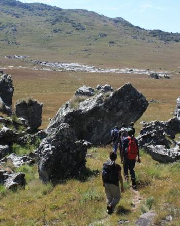 Petit groupe de personnes marchant au milieu de grands rochers déchiquetés et, en arrière-plan, de collines.