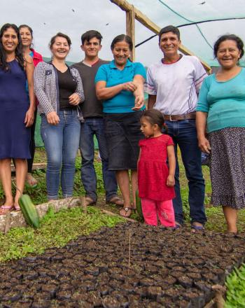 Eight people, including one small child, standing and smiling at camera within a tree nursery.