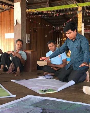 A handful of men sitting on floor around a few maps.