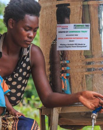Woman with young child opens a metal drum's faucet, dispensing water.