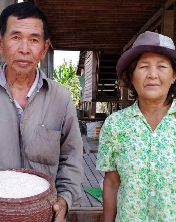 El hombre que sostiene el arroz se para al lado de la mujer. Ambos están frente a la cámara.