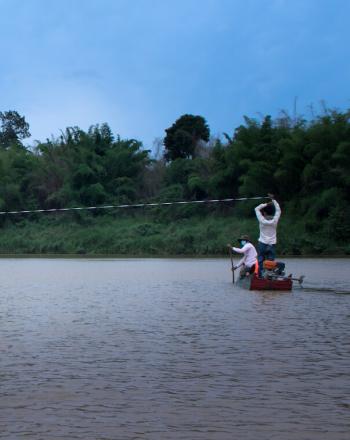 Deux petits bateaux sur l'eau, des gens debout, tenant une longue ligne tendue au-dessus de leur tête.