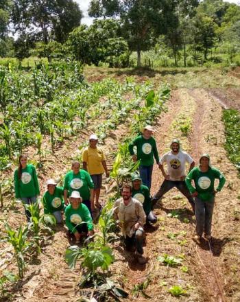 About 10 people stand in an agricultural field, smiling up at camera.