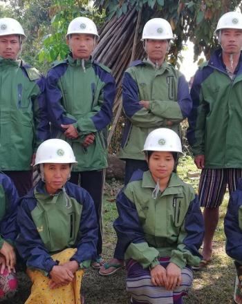 Group of 10 men and women, wearing white hard hats and matching green jackets.