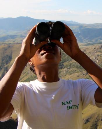Person with NAP IBITY written on shirt looking up, through binoculars.
