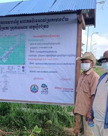 Four men standing by large signboard.