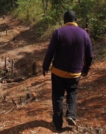 Man, back to camera, walking down bumpy dirt road.