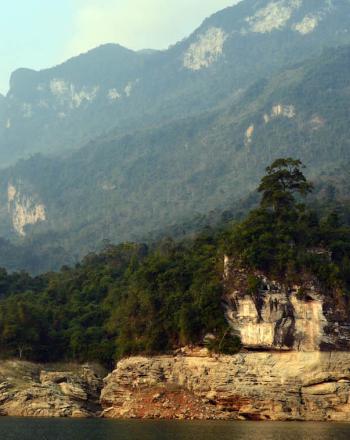 Water in foreground, karst wall and then mountains in background.