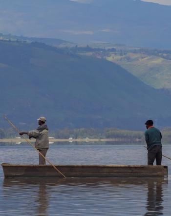 Two men standing in small boat, using long sticks to move forward.