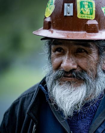少し右を向いている茶色のヘルメットをかぶった白ひげの鉱山労働者のクローズアップ。