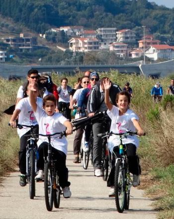 自転車に乗って道を下る子供たちのグループ、前の子供たちが笑顔でカメラに向かって手を振っています。