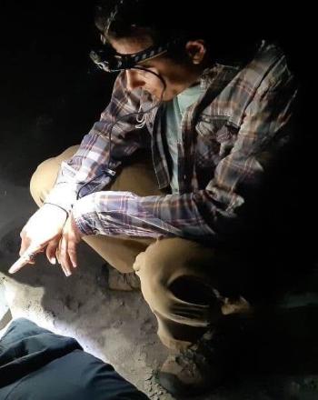 Four people wearing headlamps, crouched on ground looking at something in between them.