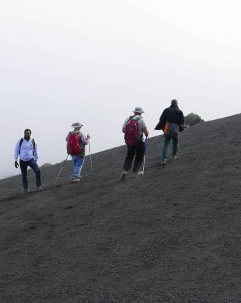 Four people climb up steep, black slope.