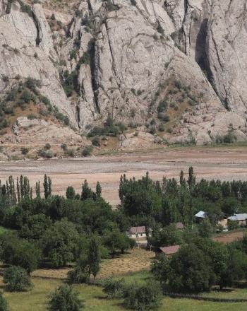 Brown river and mountains in background, small village dotted with trees in foreground