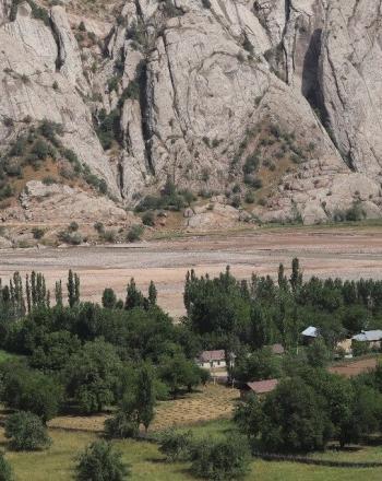 Rivière brune et montagnes en arrière-plan, petit village parsemé d'arbres en premier plan