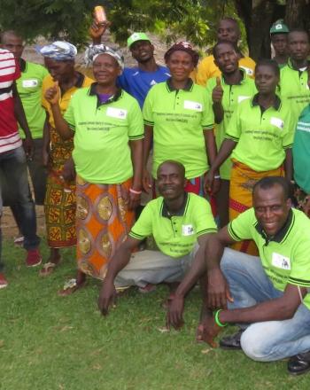 Group of about 20 people standing outside, smiling at camera. Most wear bright-green shirts.