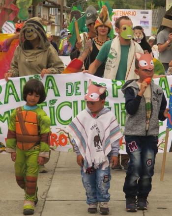 Parade of adults and children in costumes, with large banner.