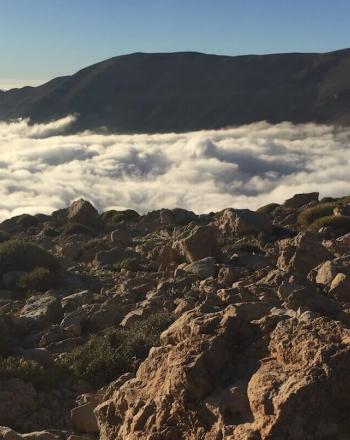 Landscape of clouds and mountains in the background, rocky ground in the foreground.