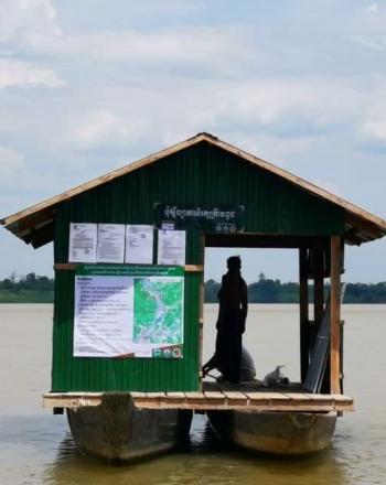 Small building held up on two large canoes. Silhouette of person standing inside.