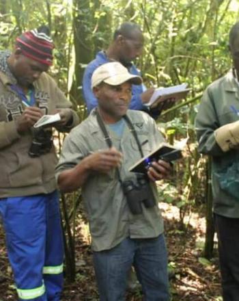 Grupo de 7 personas en bosque con libretas y binoculares.