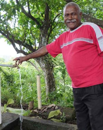 A man in an wooded area in Tafea Province, Vanuatu, uses a water spigot.