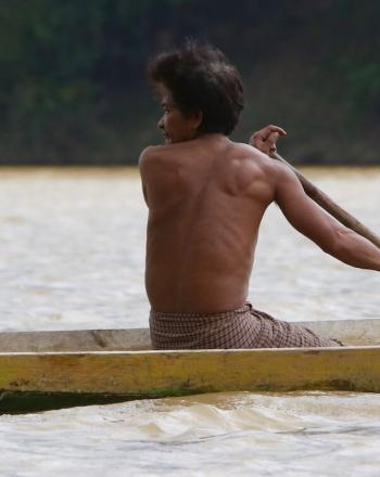 木製のカヌーを漕ぐ男が後ろを振り返る。