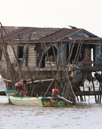 House on stilts over water, a small motorized boat with boy in front.